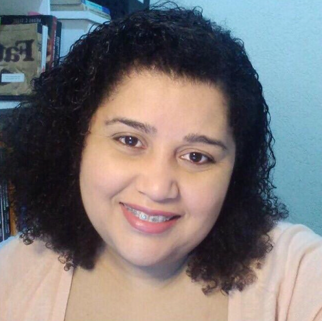 Uma mulher de cabelos cacheados está sorrindo e vestindo uma blusa rosa