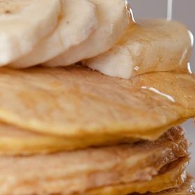 Un primo piano di una pila di pancake con fette di banana sopra.
