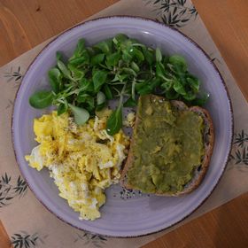 Un piatto di cibo con uova strapazzate, avocado, pane tostato e insalata su un tavolo.