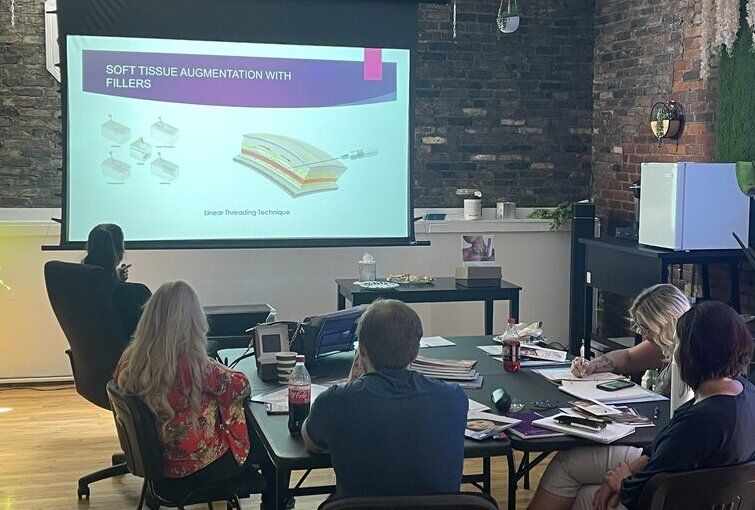 a group of people sit around a table watching a presentation about soft tissue augmentation with fillers at ERA Wellness Spa