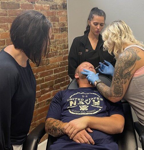 a man is getting a botox injection in his face while two women watch at ERA Wellness Spa
