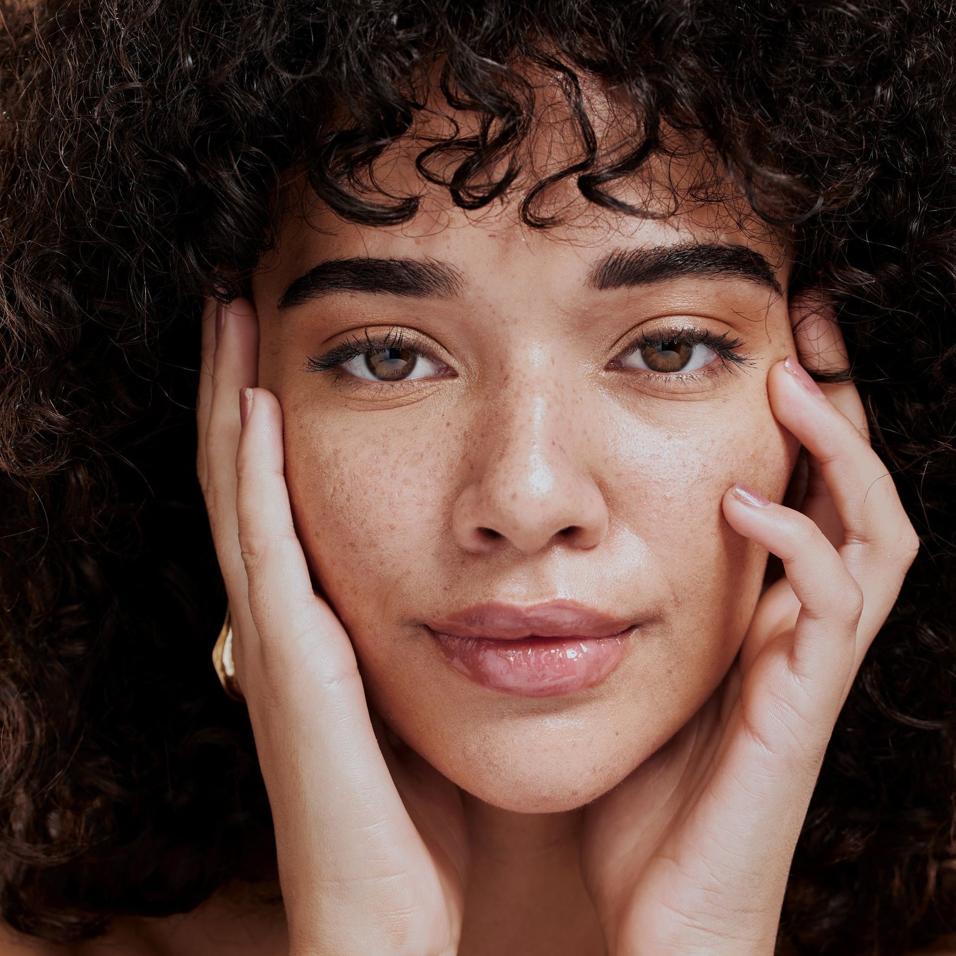 a woman with curly hair touches her face with her hands at ERA Wellness Spa