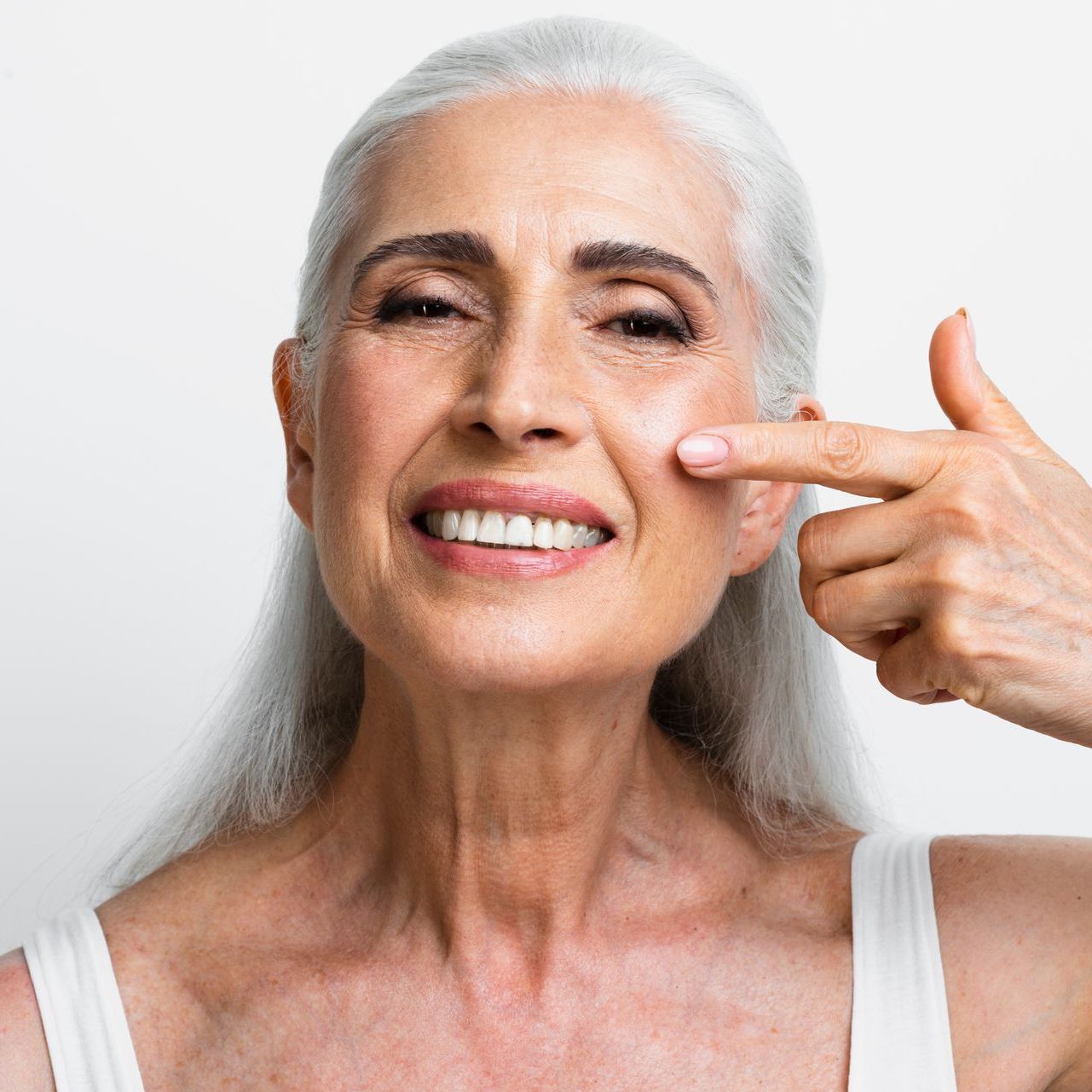 a woman with gray hair is smiling and pointing at her face at ERA Wellness Spa