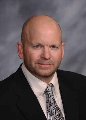 A bald man in a suit and tie is smiling for the camera.