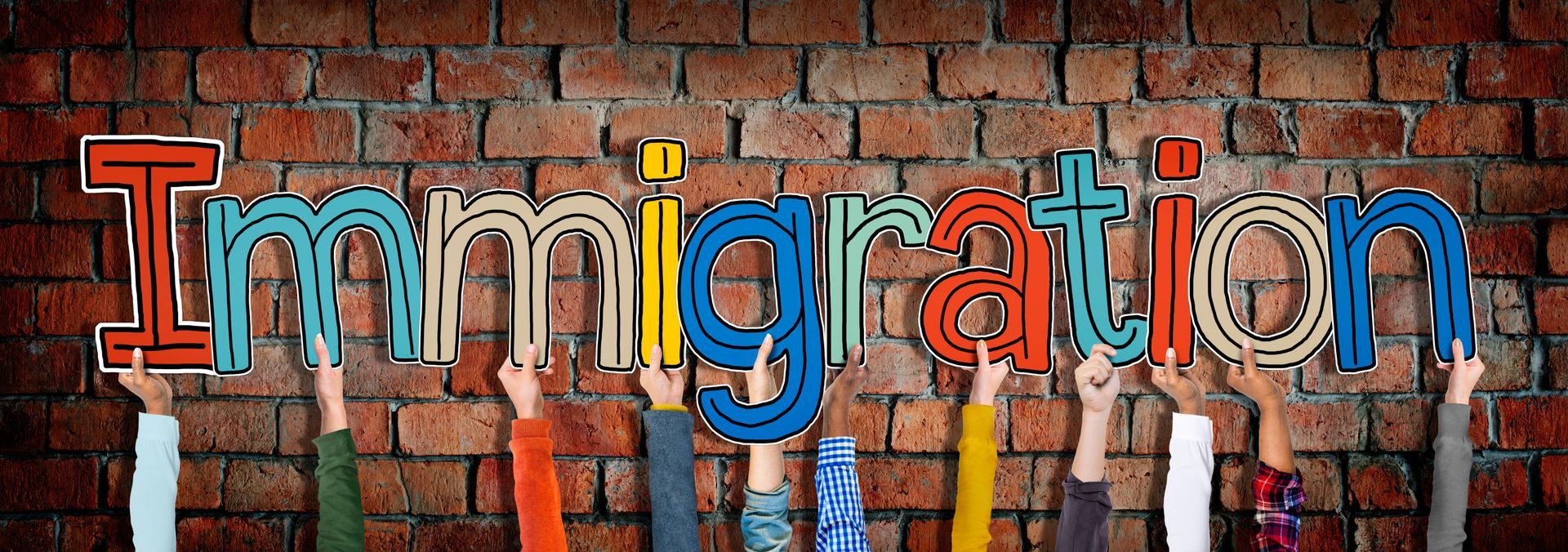A group of people are holding up the word immigration on a brick wall.