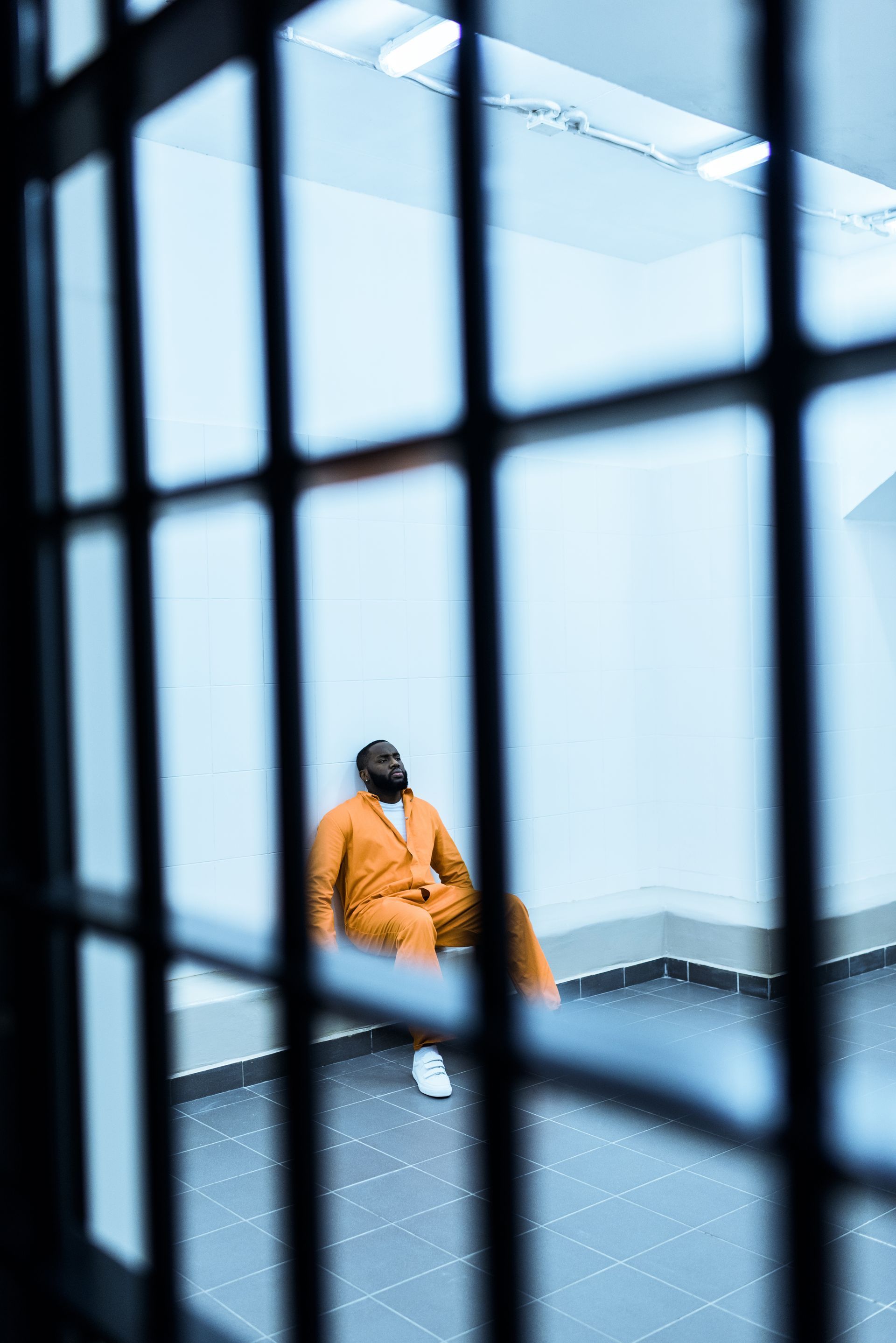 A man in an orange suit is sitting in a cell behind bars.