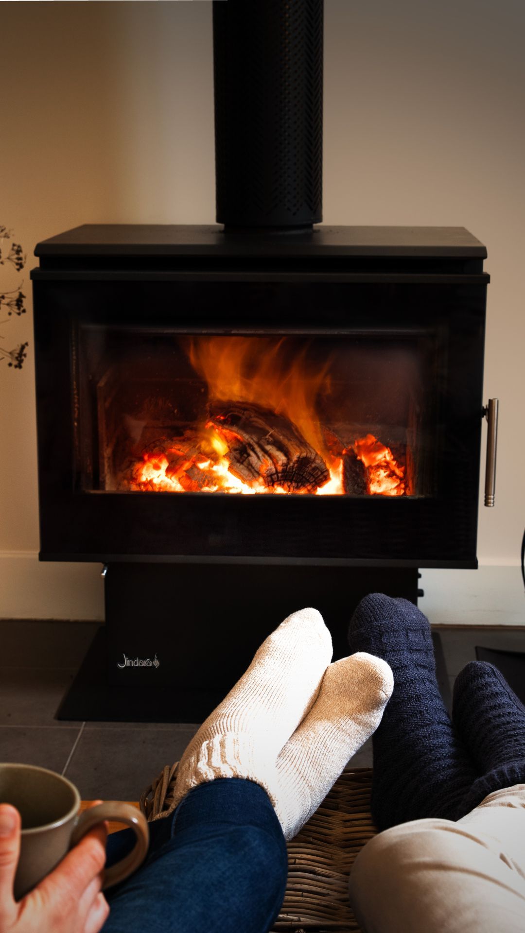 A person is sitting in front of a fireplace with their feet up.