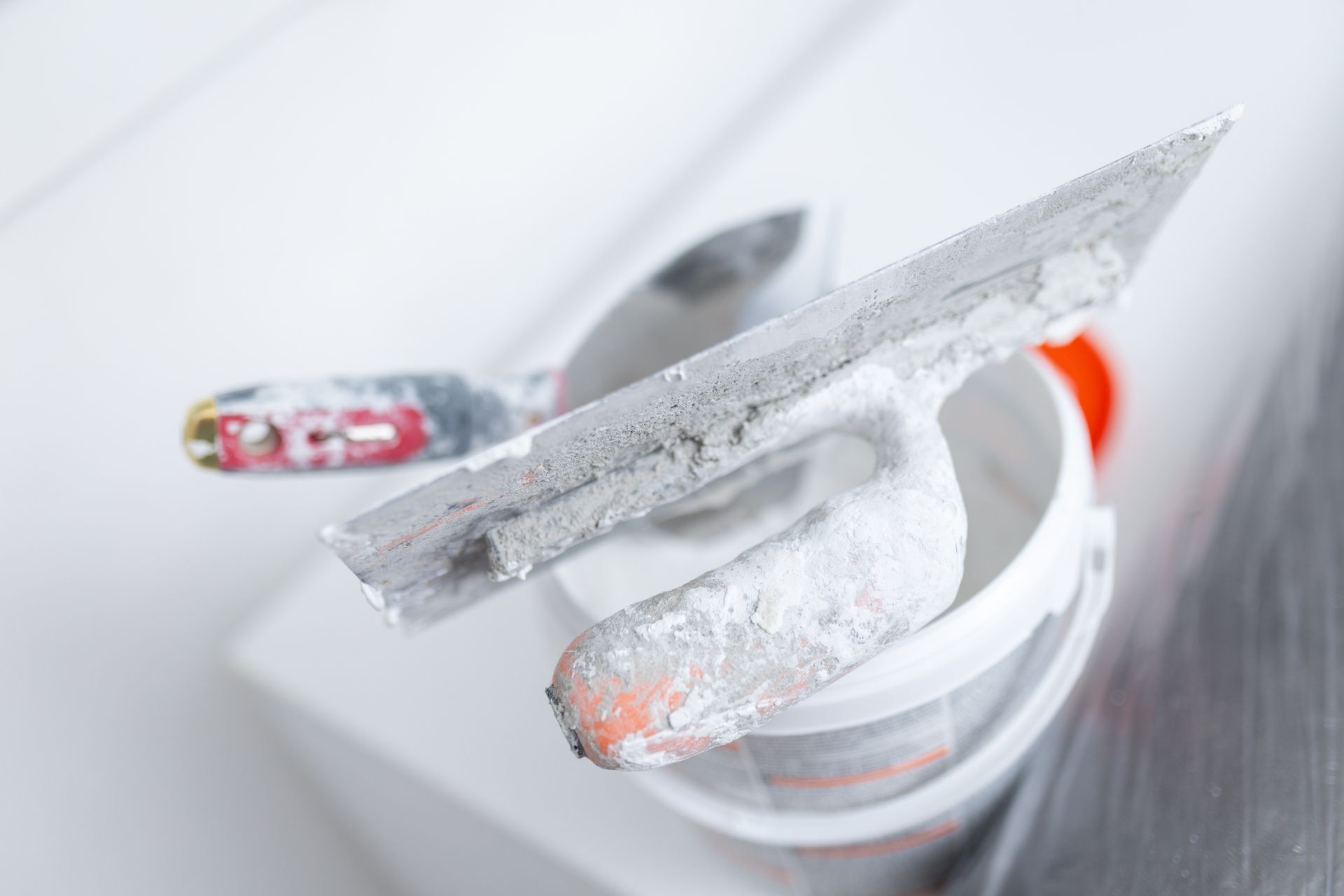 A trowel is covered in joint compound resting on a bucket.