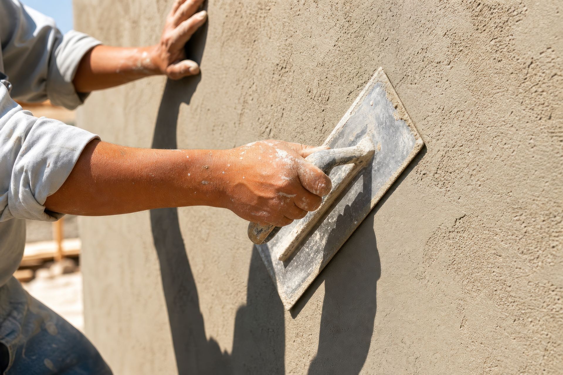 Professional builder applying wet plaster to concrete wall with metal trowel Professional builder applying wet plaster to concrete wall with metal trowel