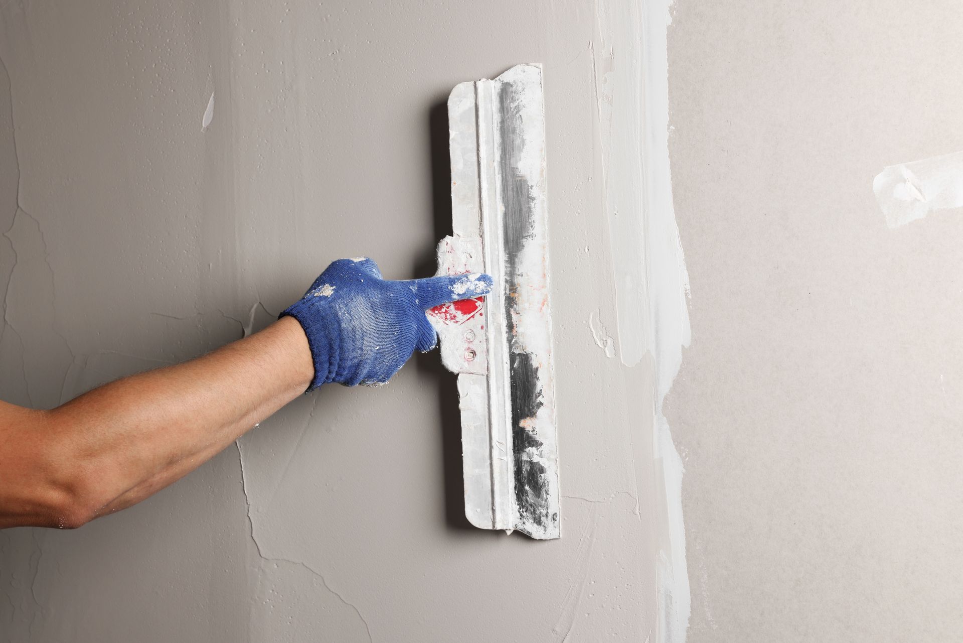 The arm of a professional worker plastering a wall with a putty knife.