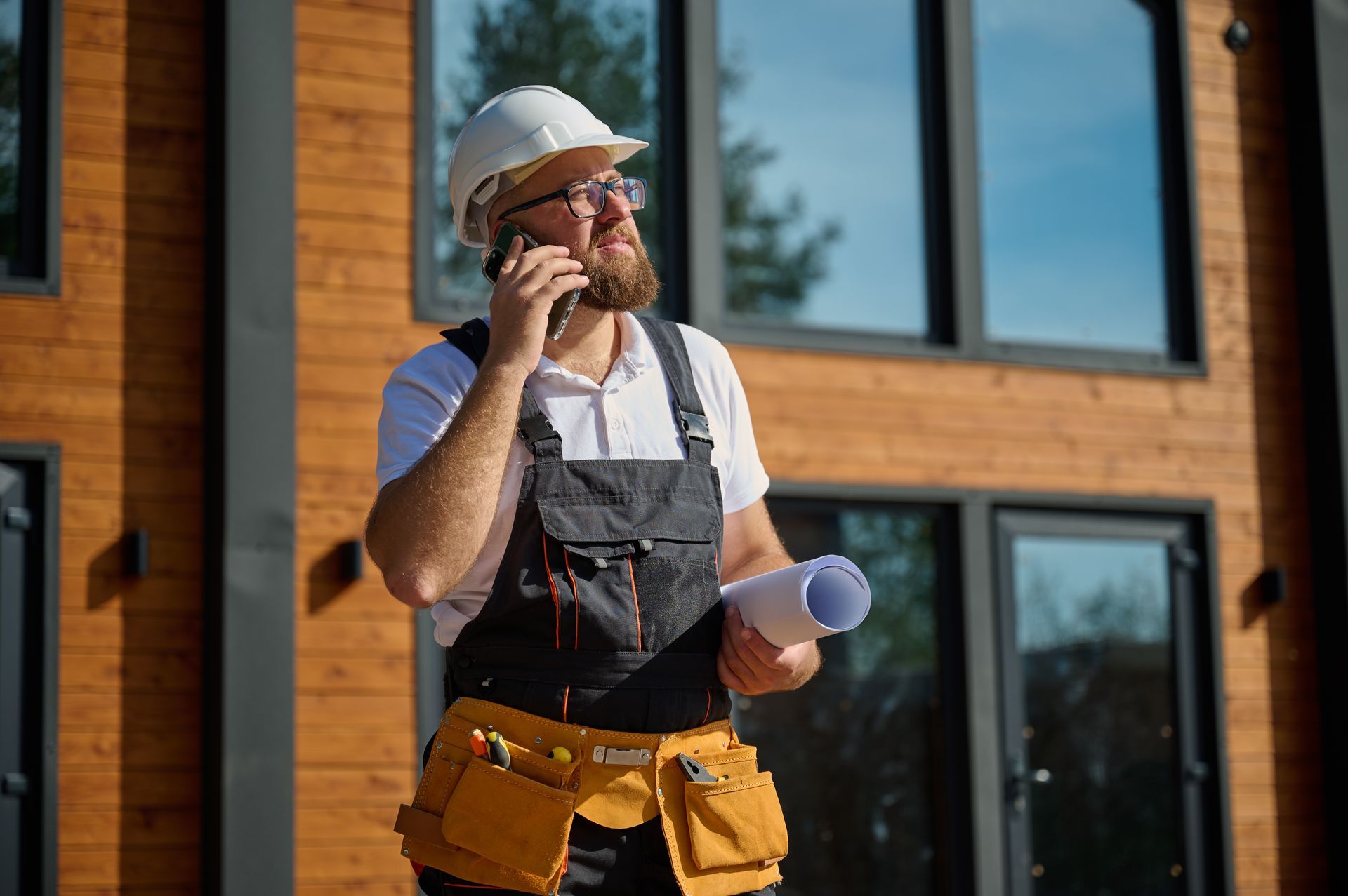 Un ouvrier du bâtiment parle au téléphone portable tout en tenant un plan.