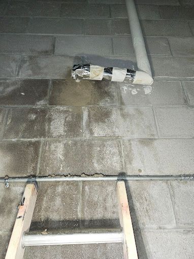 A ladder is sitting next to a pipe on a brick floor.