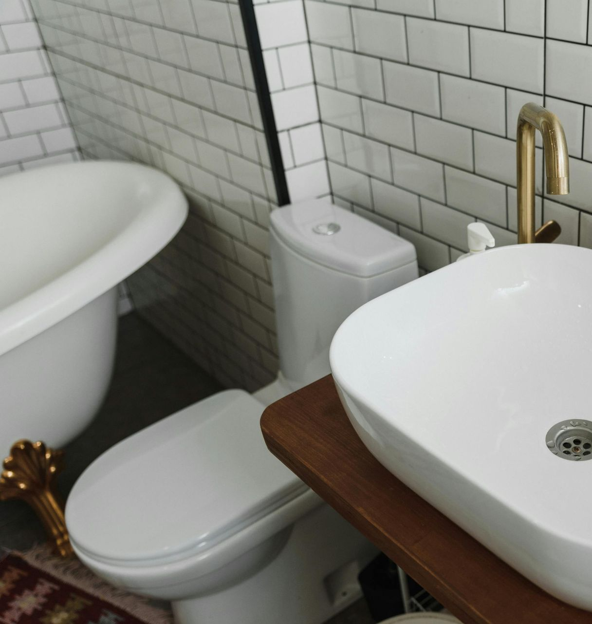 Bathroom with white fixtures, including a tub, toilet, and sink. Brick-patterned white tile wall. Wooden countertop.
