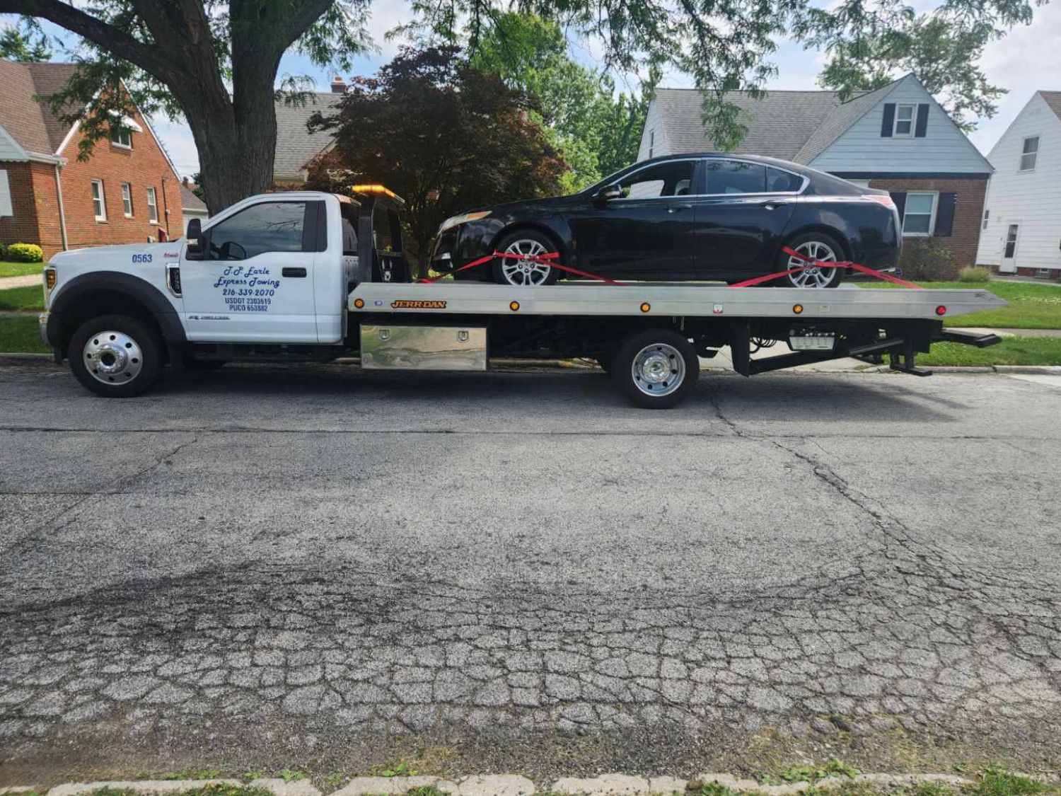 Tow truck with a black car on the flatbed, on a residential street.