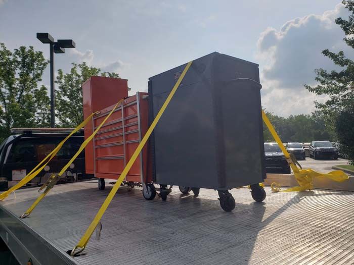 Two toolboxes secured on a flatbed tow truck with yellow straps.