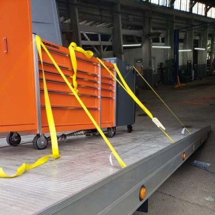 Orange tool chest secured with yellow straps on a flatbed trailer in a garage.