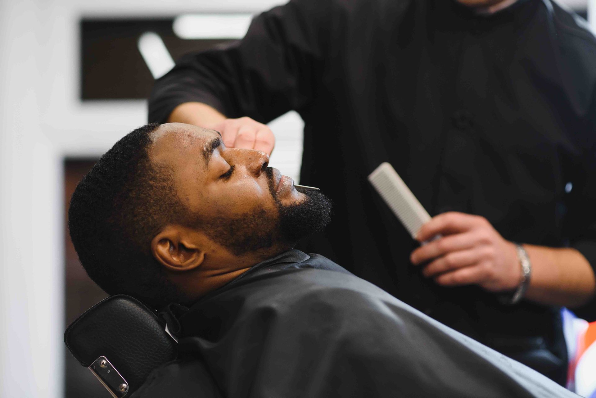A man is getting his beard shaved by a barber in a barber shop.