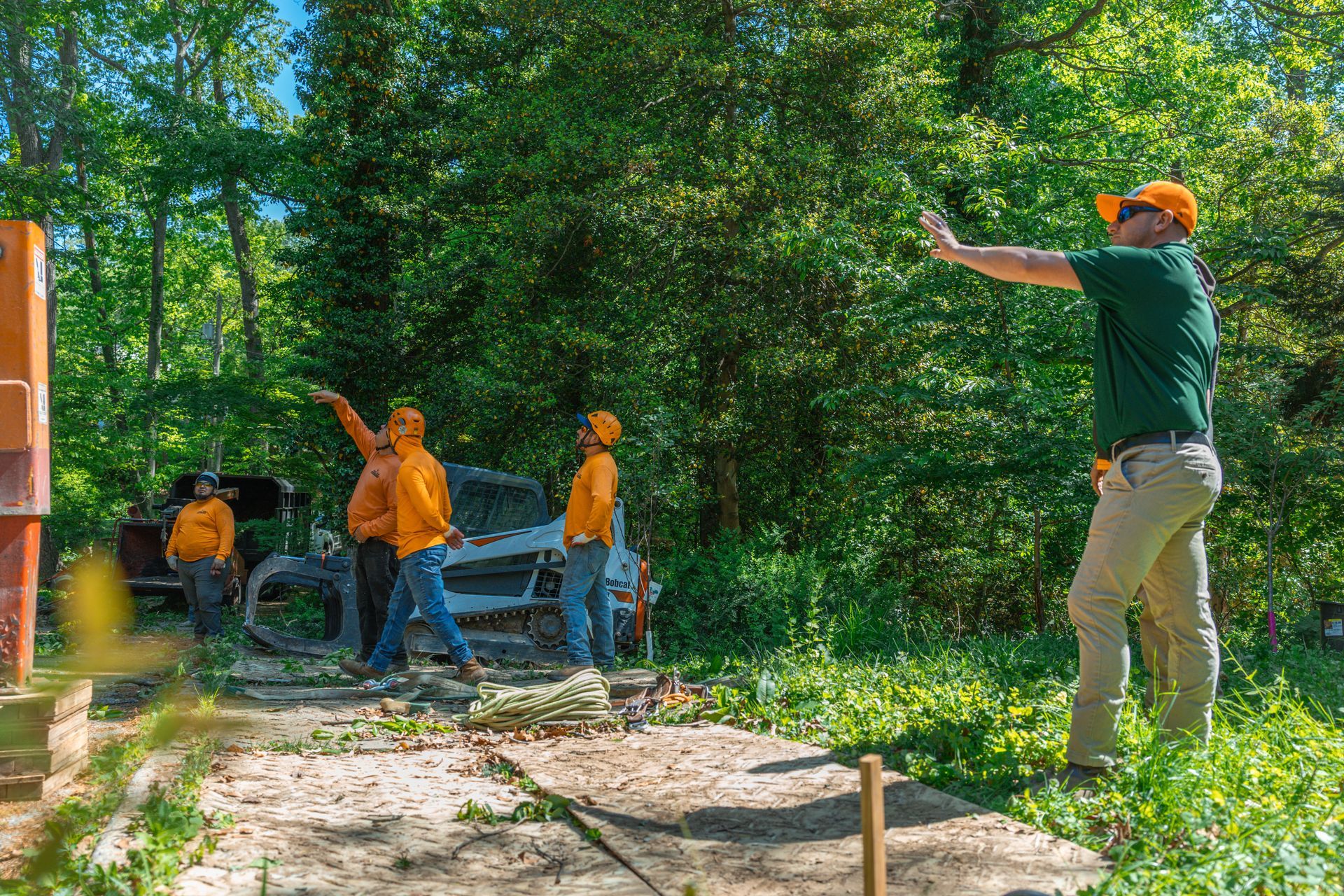 Workers in orange and green gear clearing debris in a wooded area near a truck