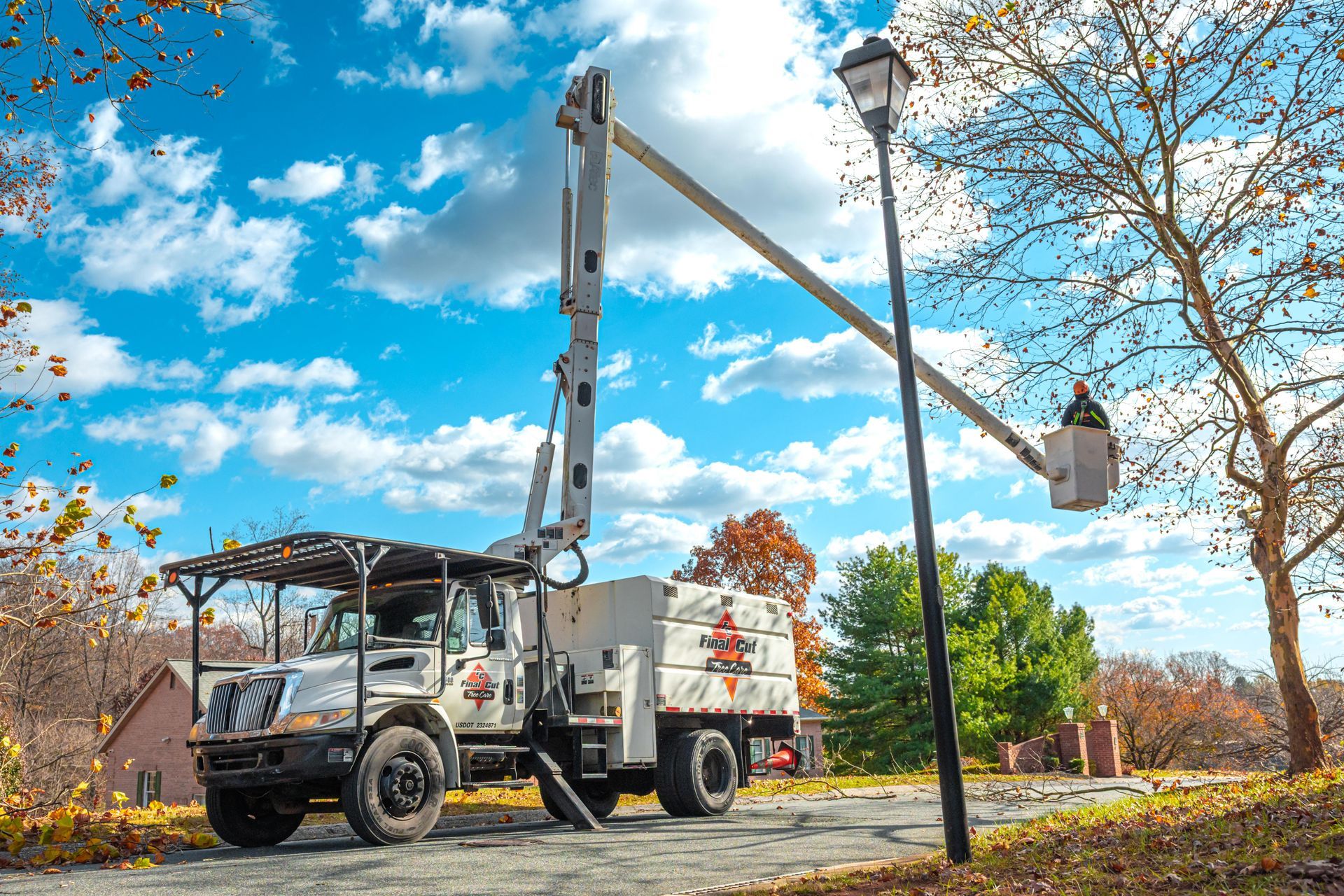 A truck with an extended lift arm servicing a street lamp on a road, blue sky with clouds.