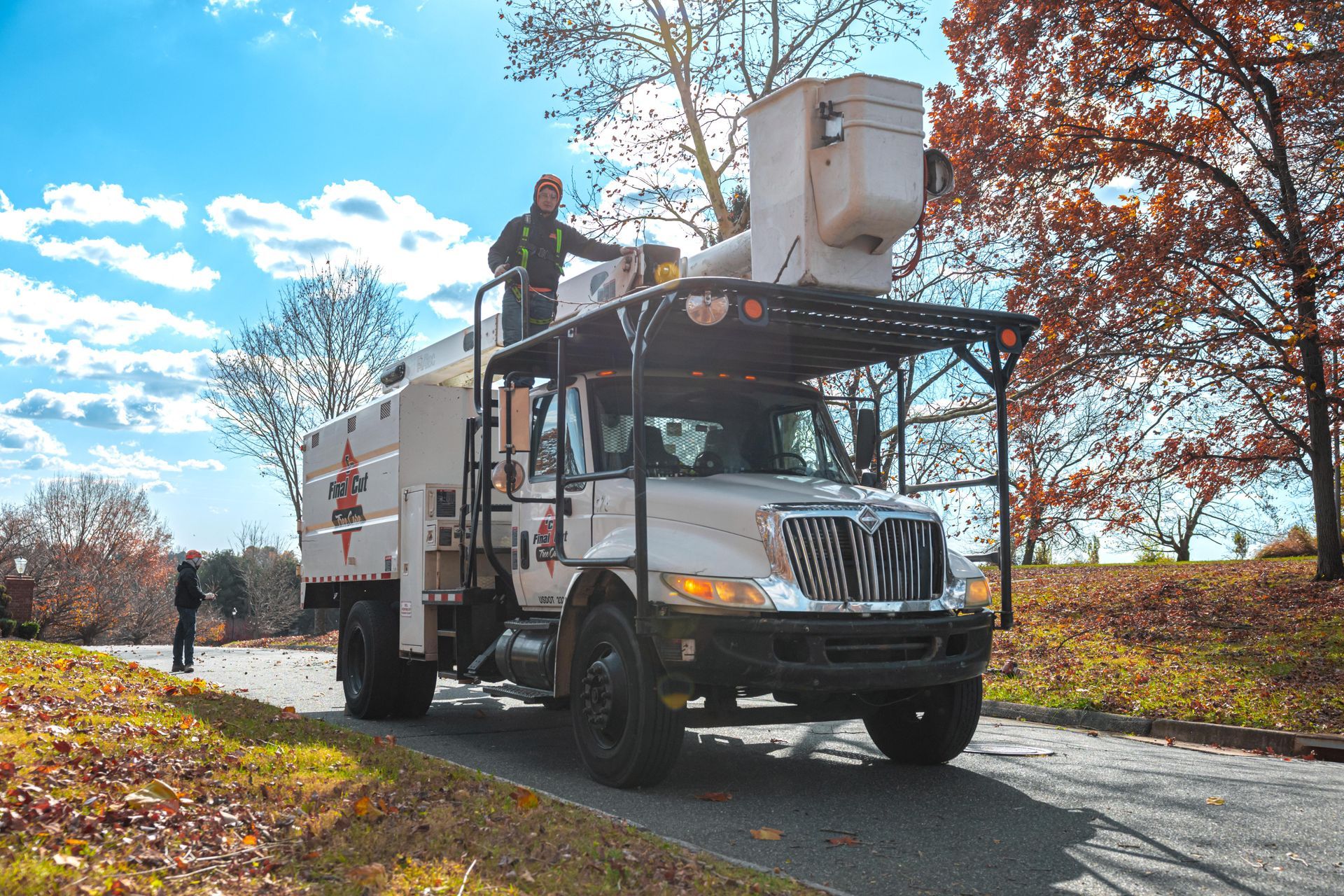 Man operating an aerial lift truck to trim trees on a sunny day.