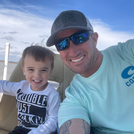 Man and child smiling on a boat, man in sunglasses and hat, child wearing a