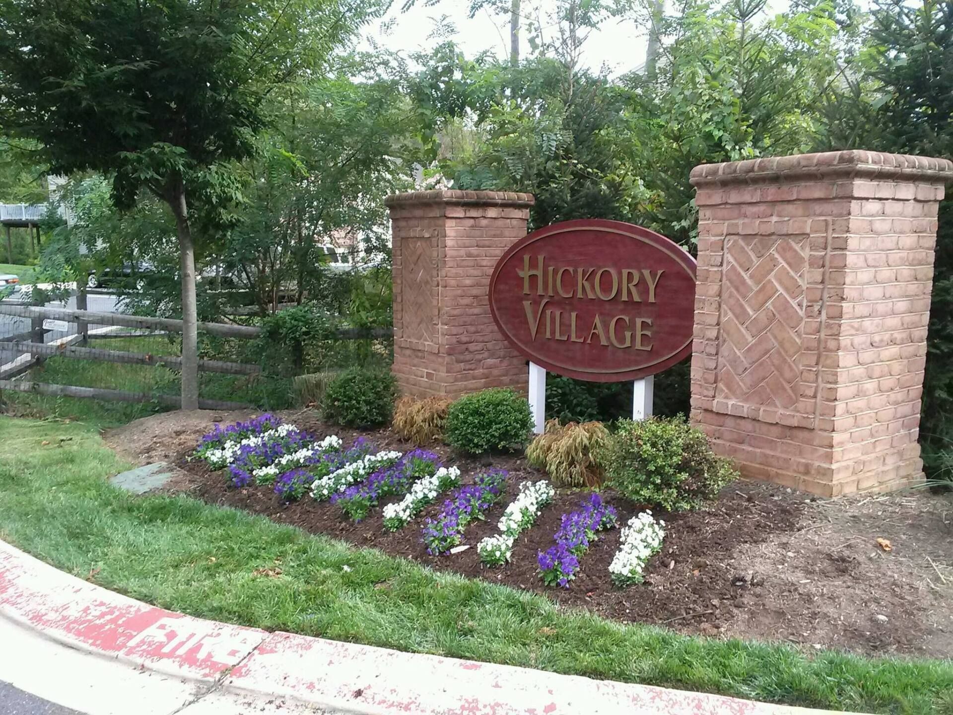 Sign for Hickory Village with brick columns, surrounded by flowers and greenery.