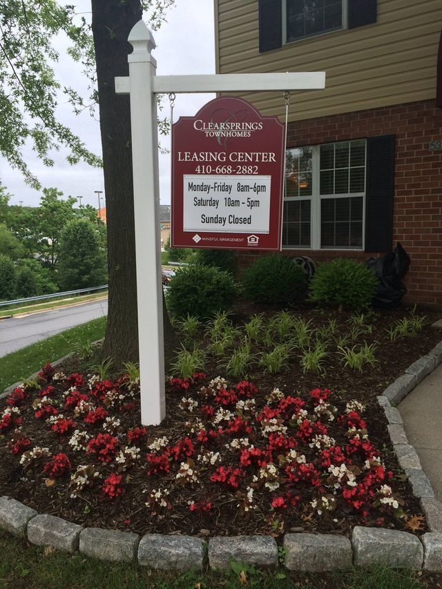 Sign for a leasing center with hours listed, surrounded by red and white flowers.