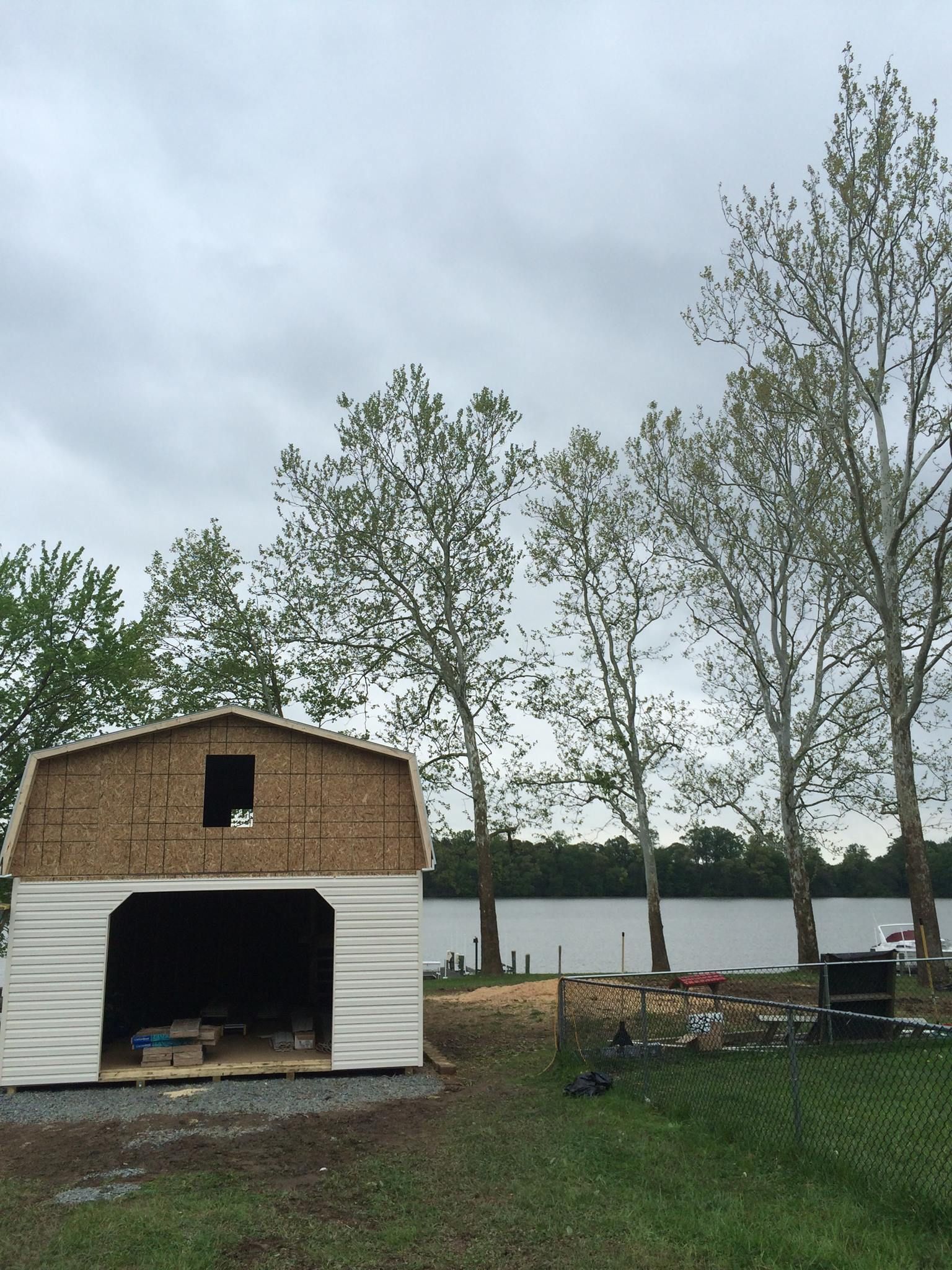 A partially built shed with an open doorway, near a body of water and trees under a cloudy sky.