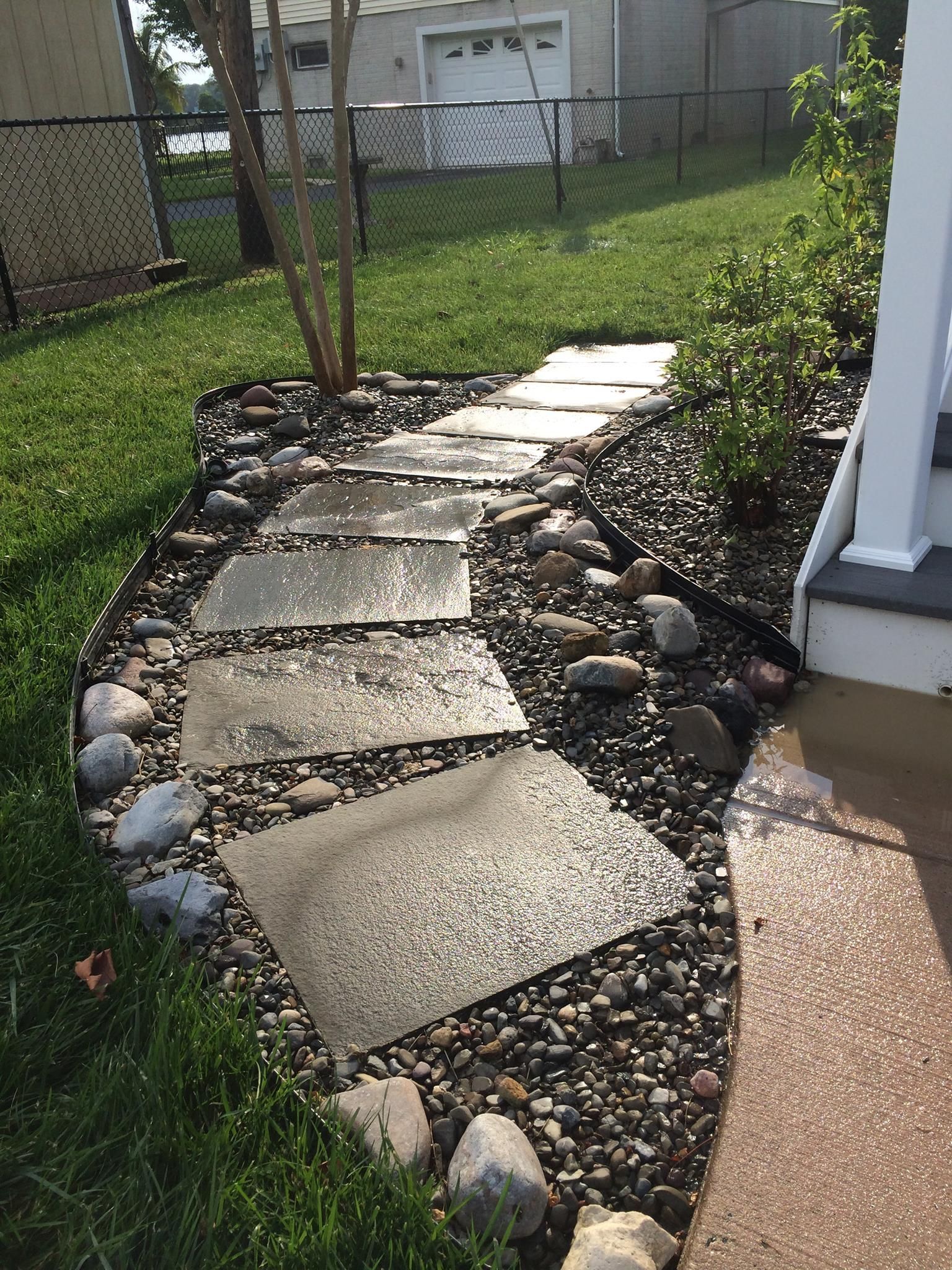 Stone pathway through gravel and grass near a white porch.