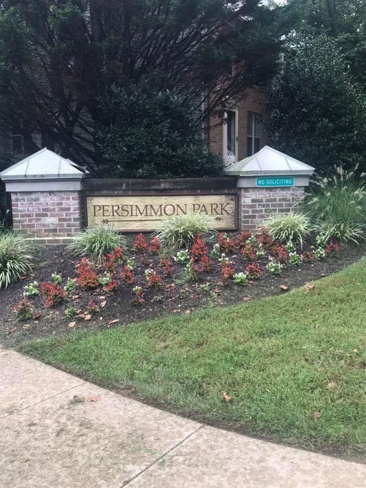 Sign for Persimmon Park with brick pillars, floral landscaping, and green grass.