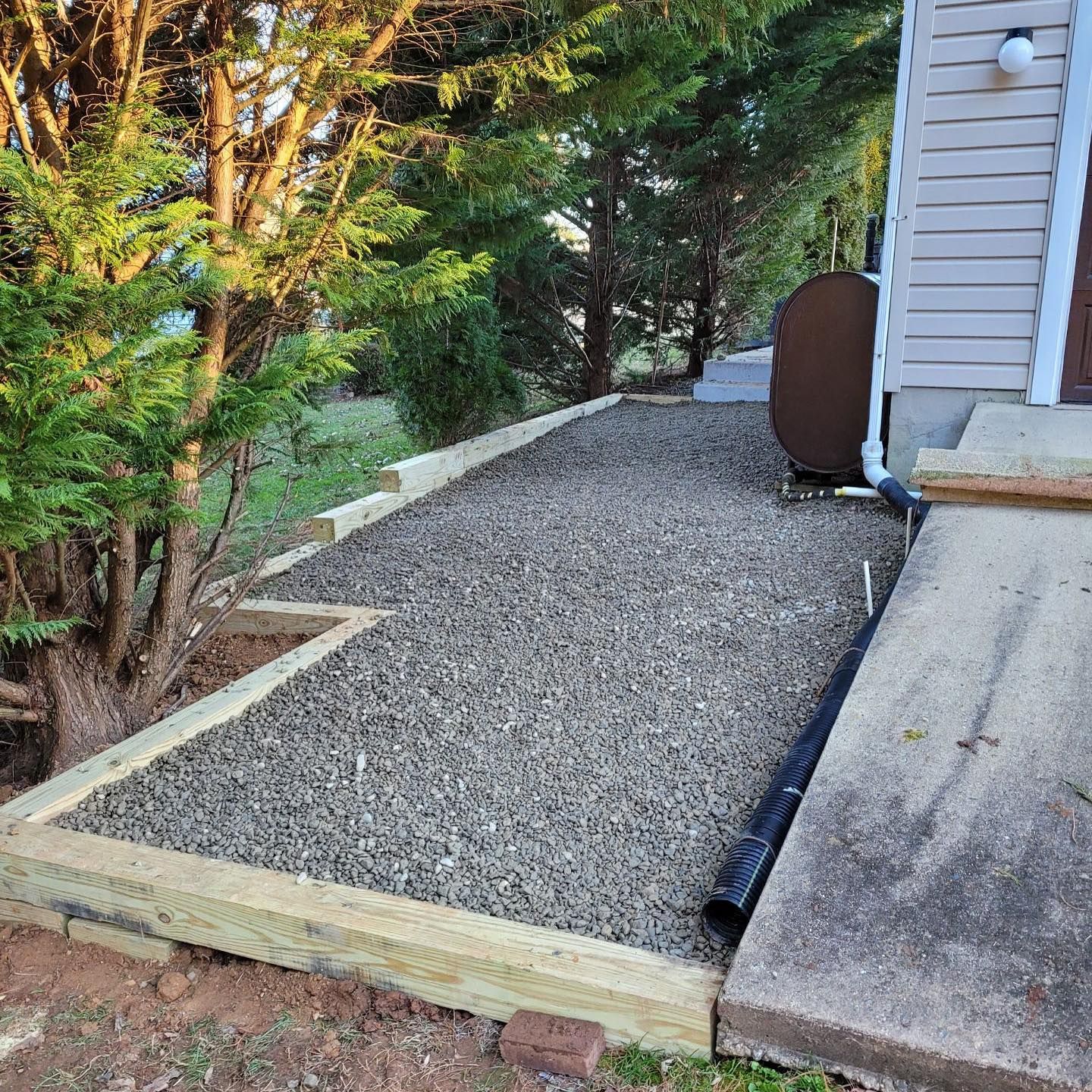 Gravel pathway next to a building, bordered by wooden beams. Trees and bushes surround the area.