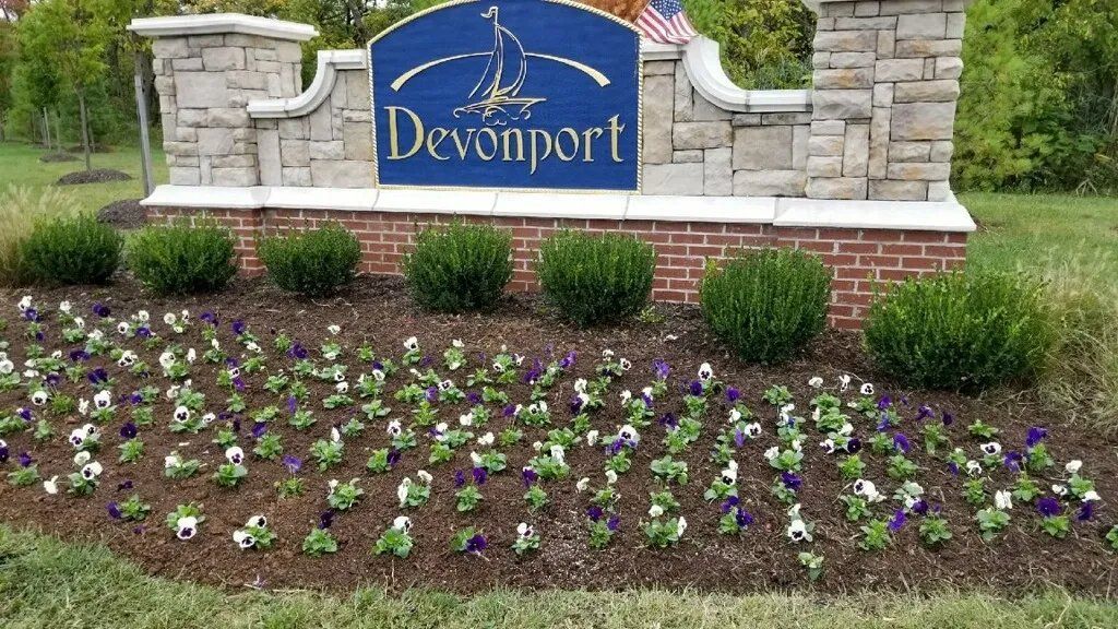 Sign for Devonport with stone and brick, surrounded by flower bed of white and purple pansies.