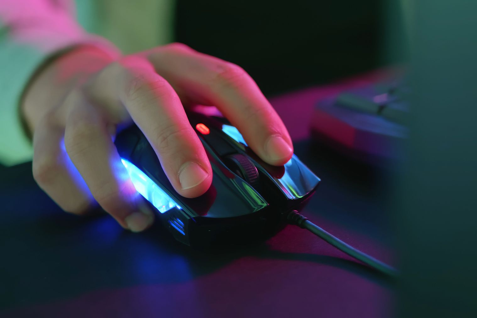 A hand resting on a computer mouse next to a keyboard.