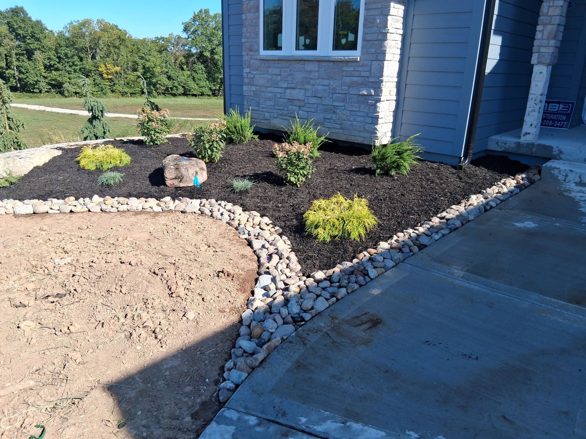 Front yard landscaping with rocks, mulch, and plants next to a house with a blue exterior.