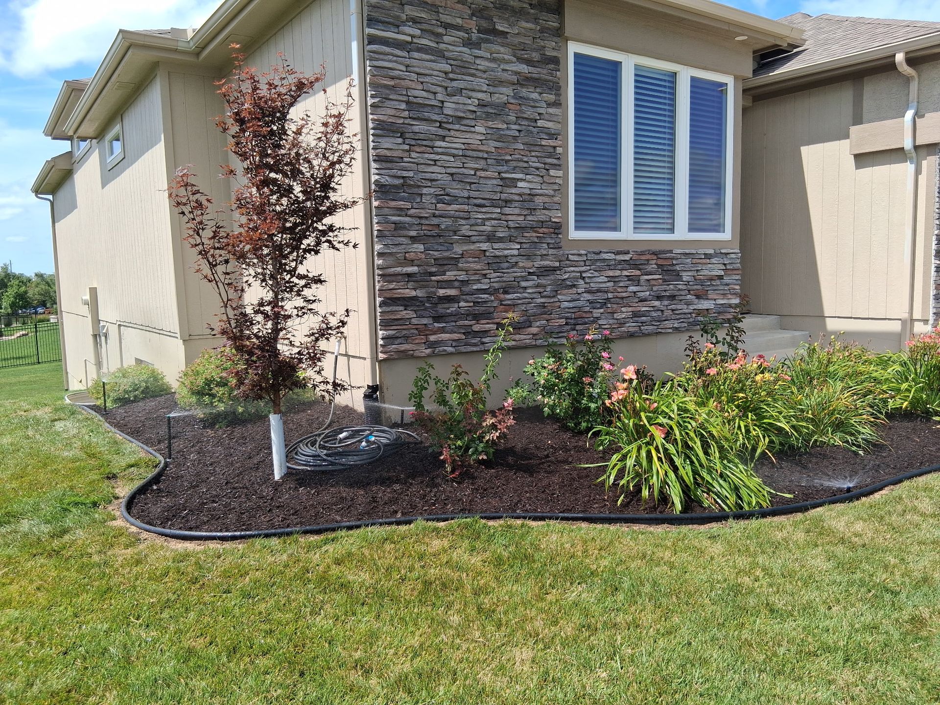 House exterior with landscaping: tan siding, stone accent, flower bed with dark mulch, and green grass.