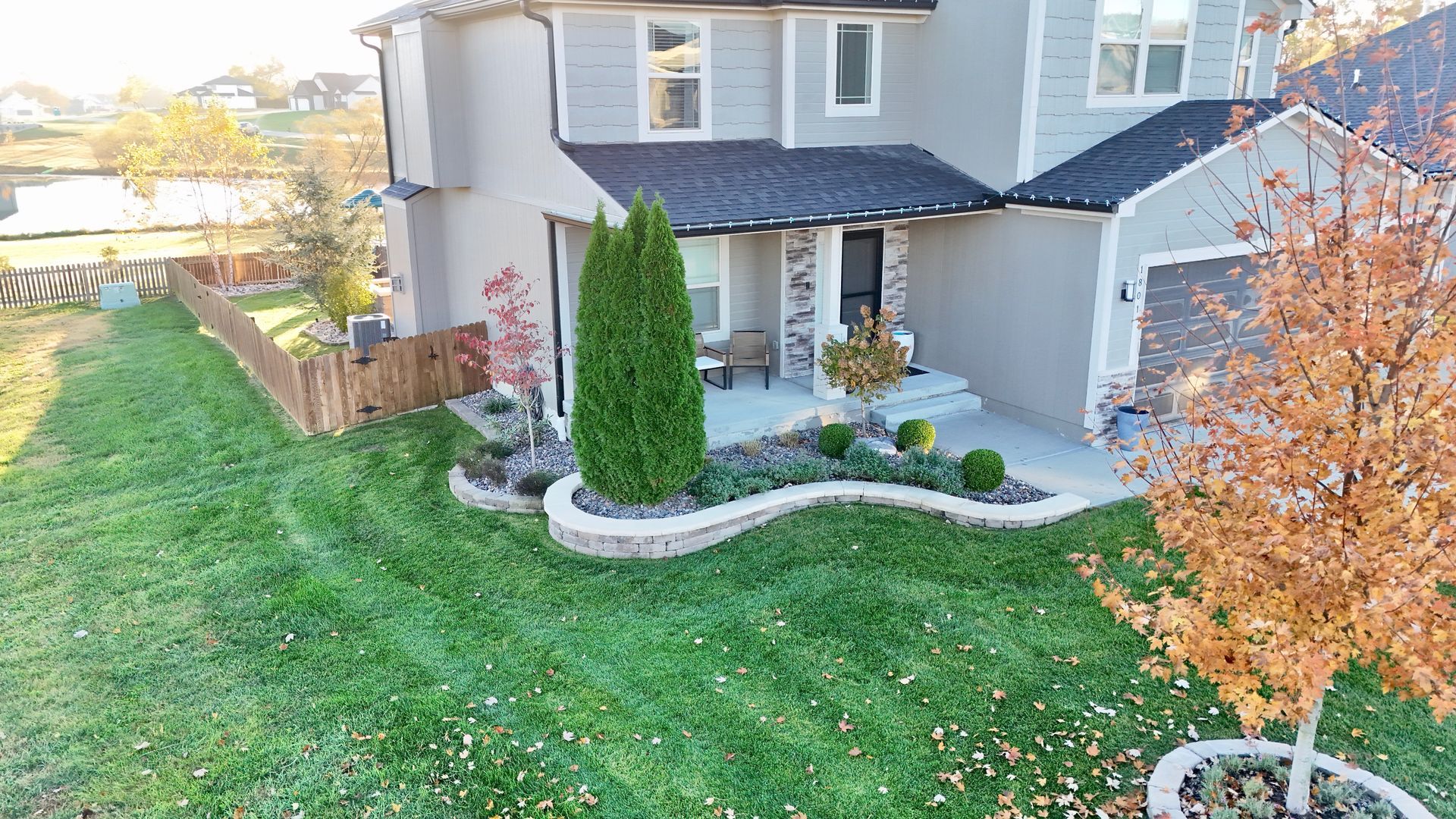 Two-story house with green lawn and landscaping; a small tree with orange leaves.