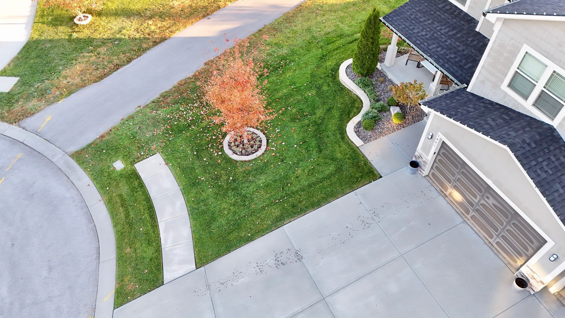 Aerial view of a house with a gray exterior, driveway, and a lawn with a small tree.