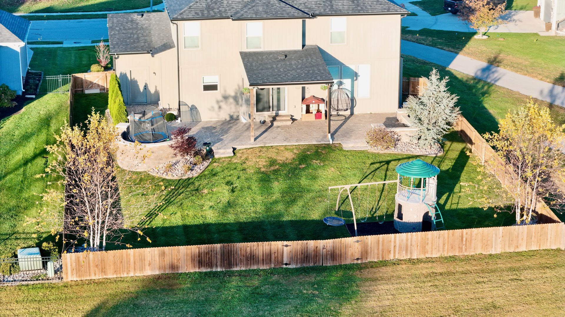 Backyard with house, patio, wooden fence, play structure, and green grass.