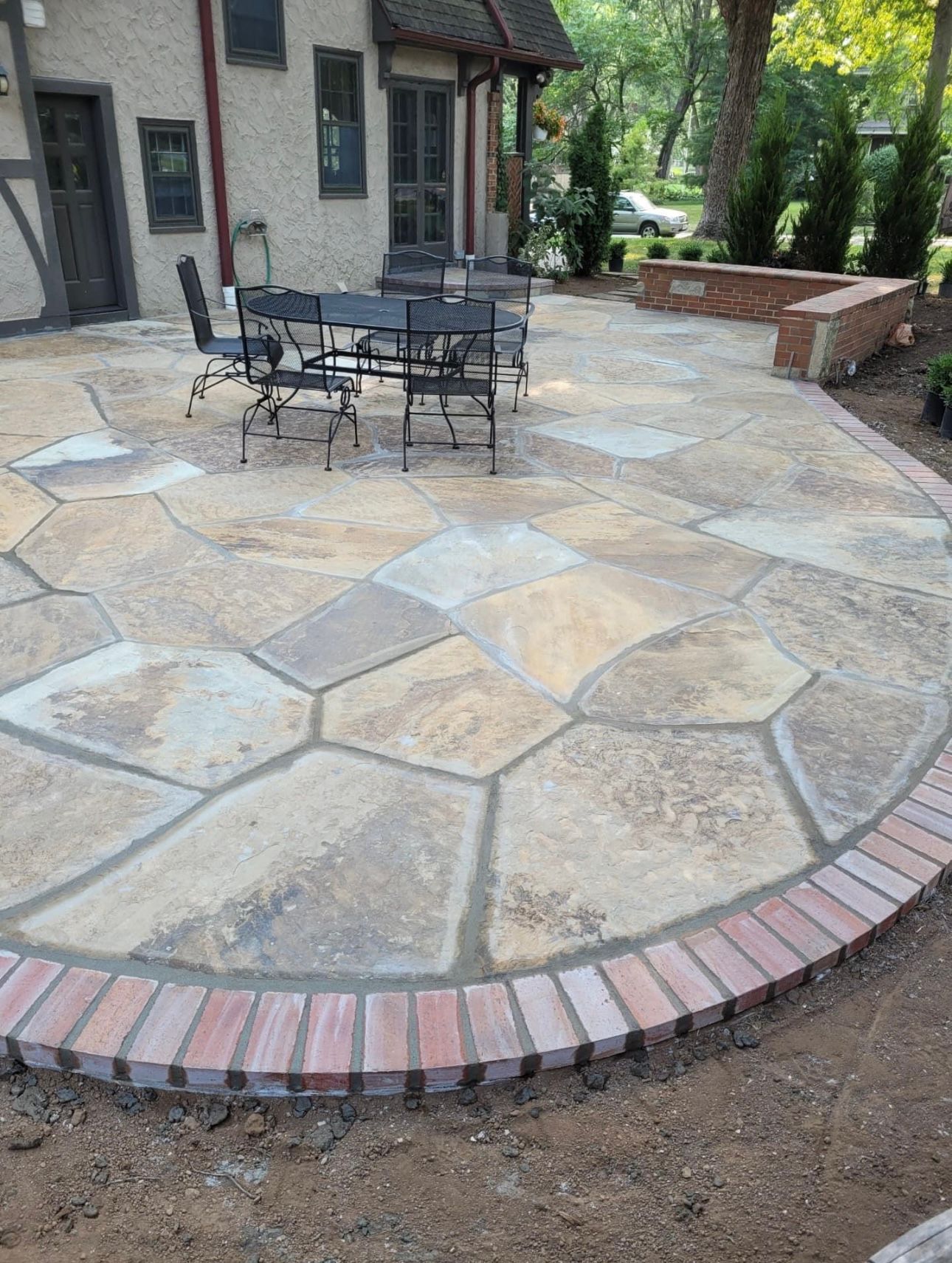 Patio with irregular stone and brick border; black table and chairs set.