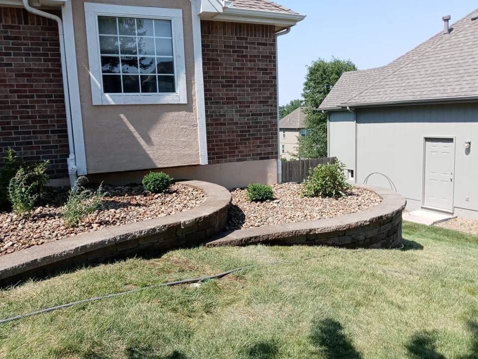 A brick house with a curved retaining wall filled with mulch and plants, on a sunny day.