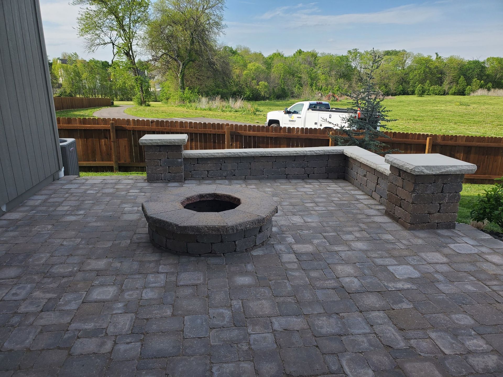 Stone patio with fire pit, seating wall, and wooden fence in a yard.