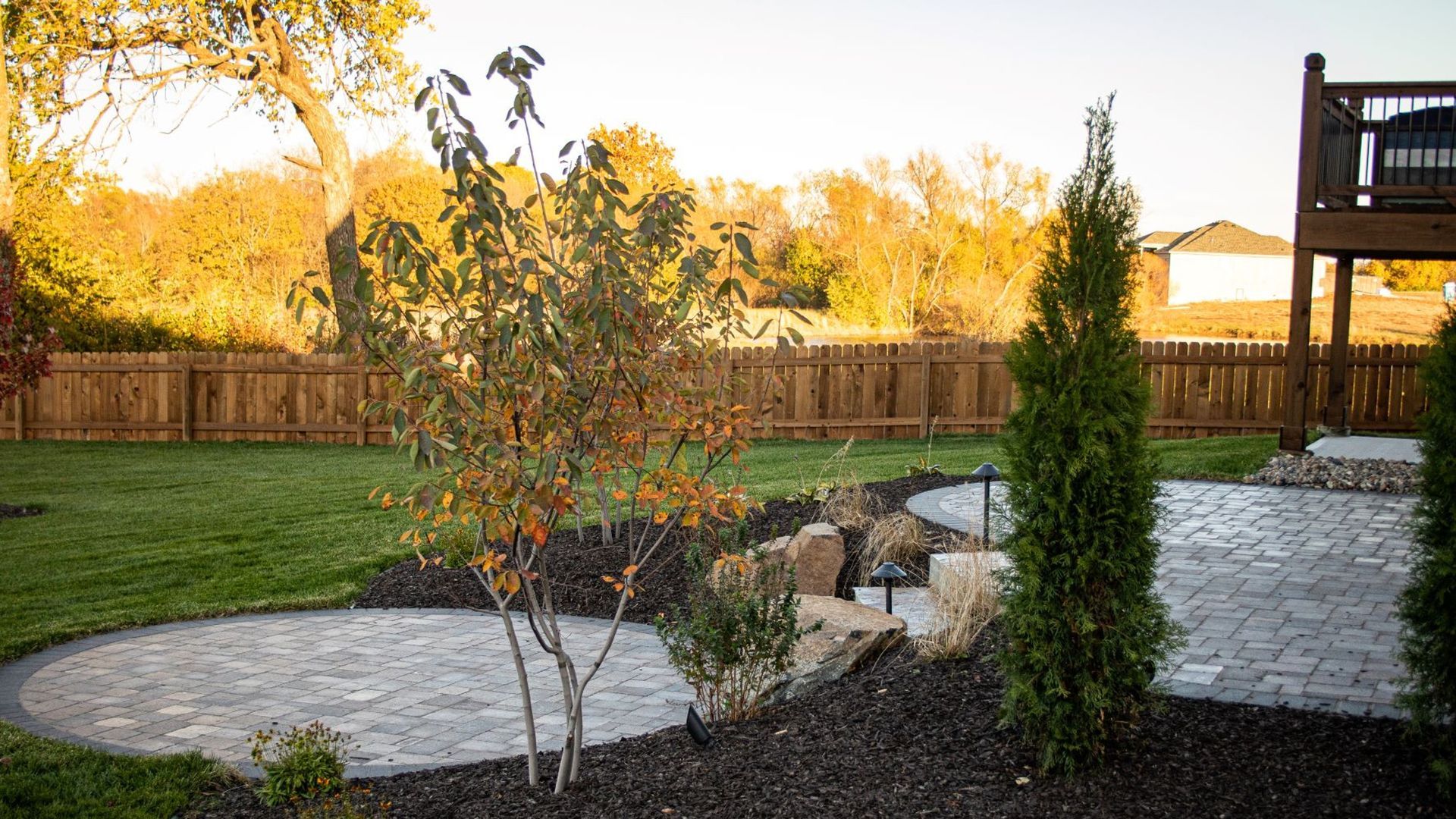 Backyard patio with a circular stone area, plants, and a wooden fence.