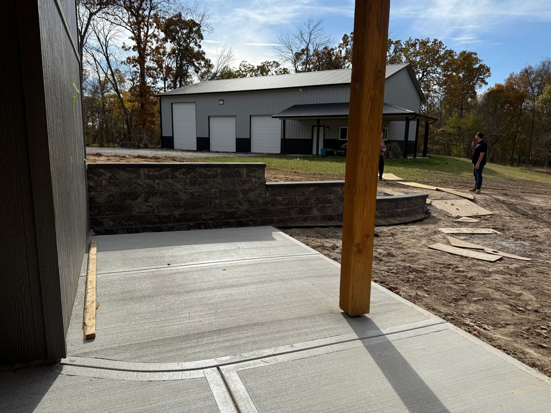 New concrete patio with a retaining wall and building in the background. A person stands nearby.
