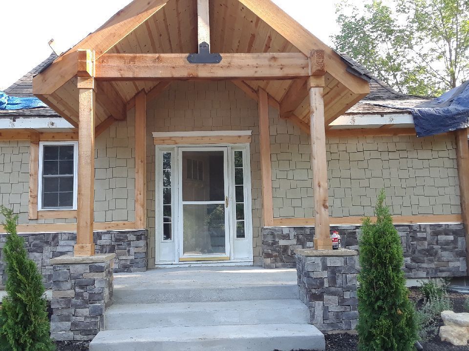 House under construction with stone columns, wood porch, and steps leading to the front door.