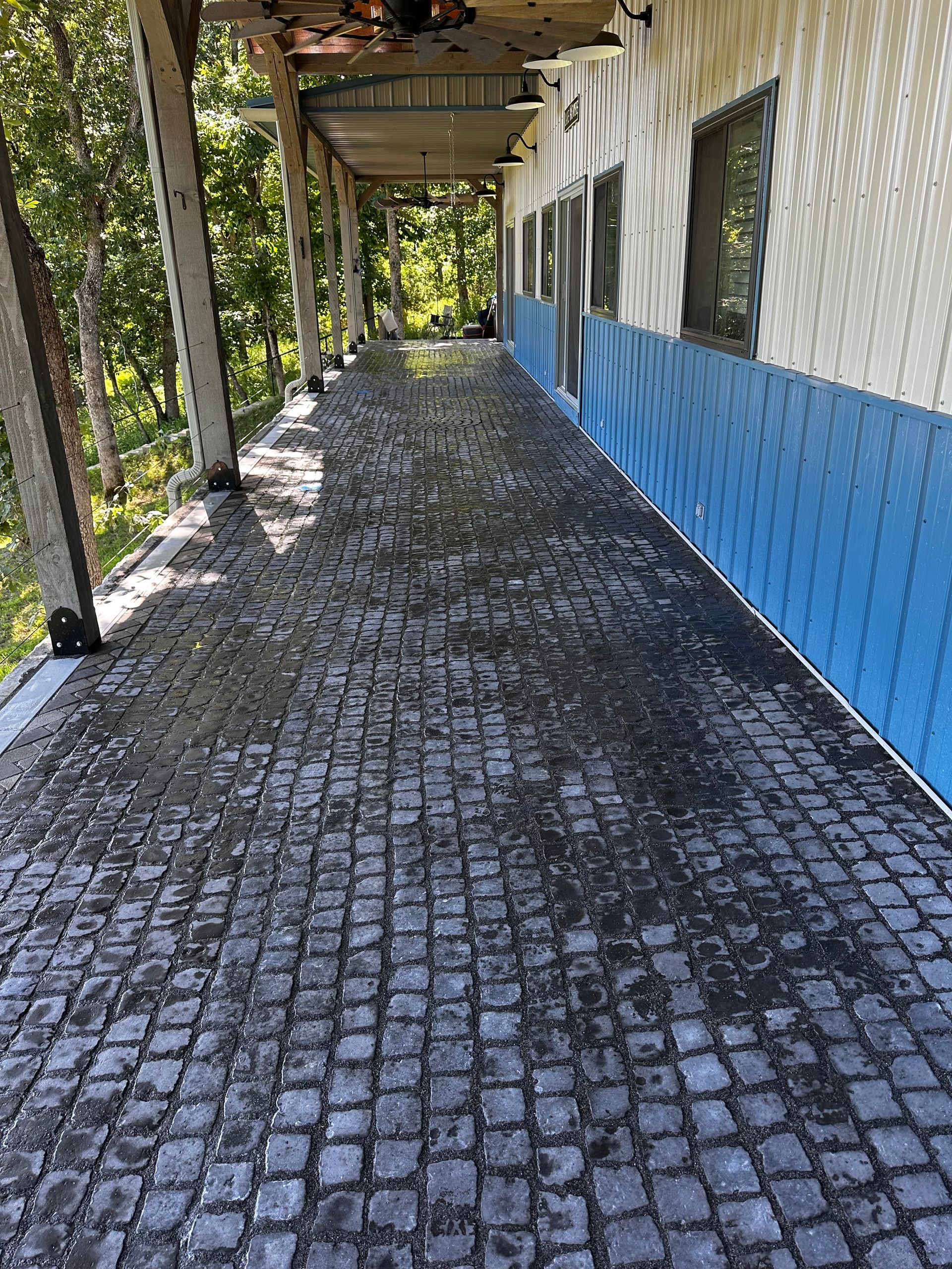 Covered walkway with cobblestone floor. Blue and white wall on the right, supported by columns.