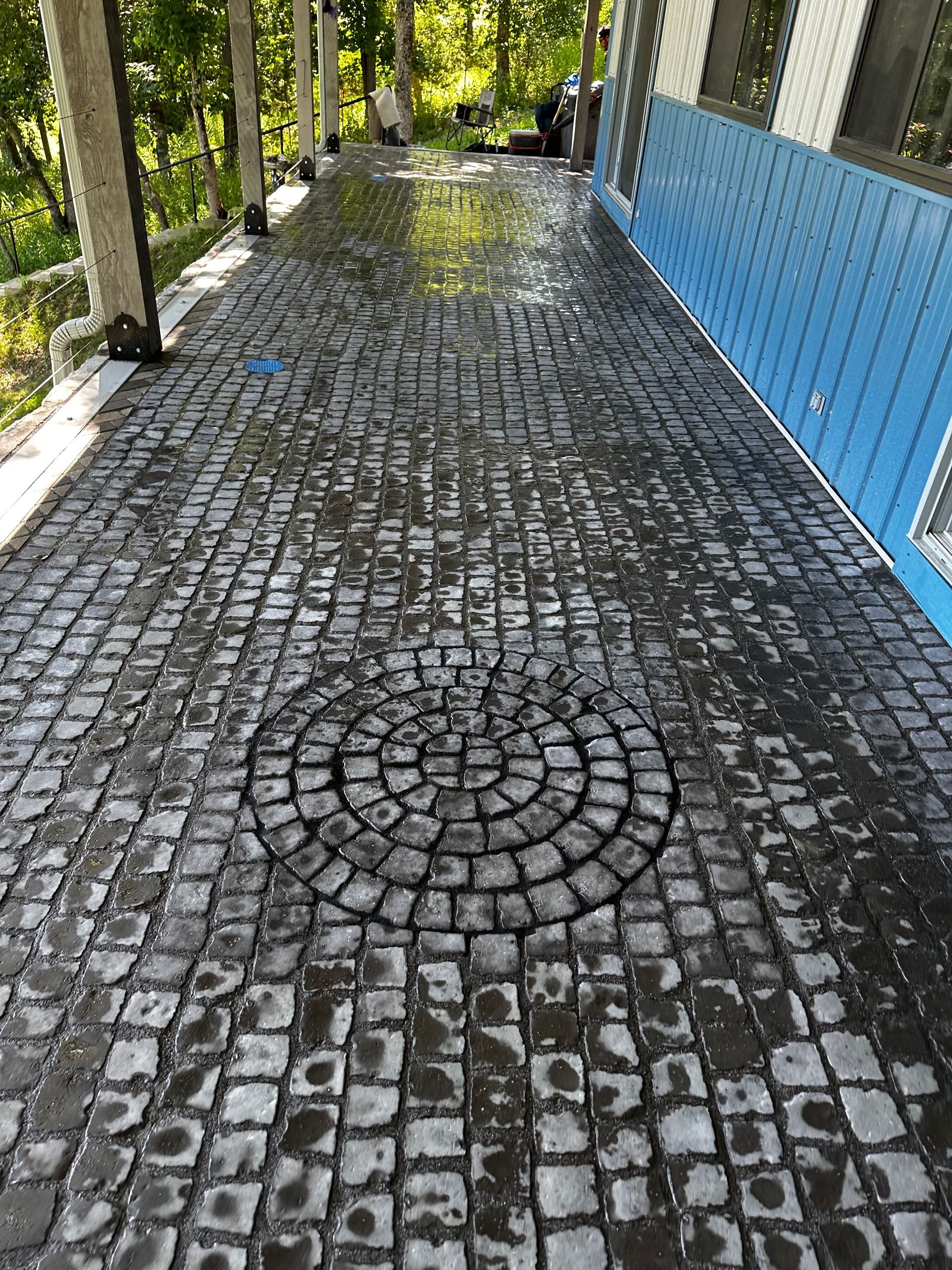 Wet cobblestone patio with circular design feature next to a blue building.