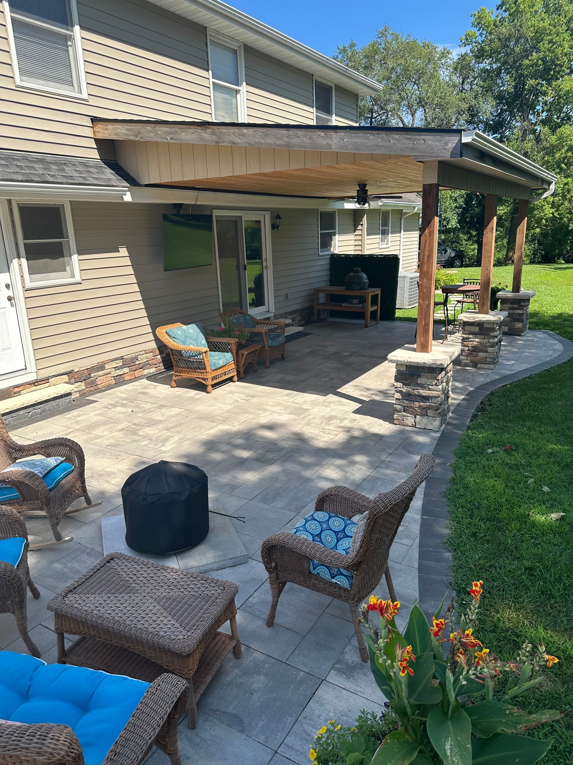 Patio with seating under a wooden pergola, leading to a lawn, and the house in the background.
