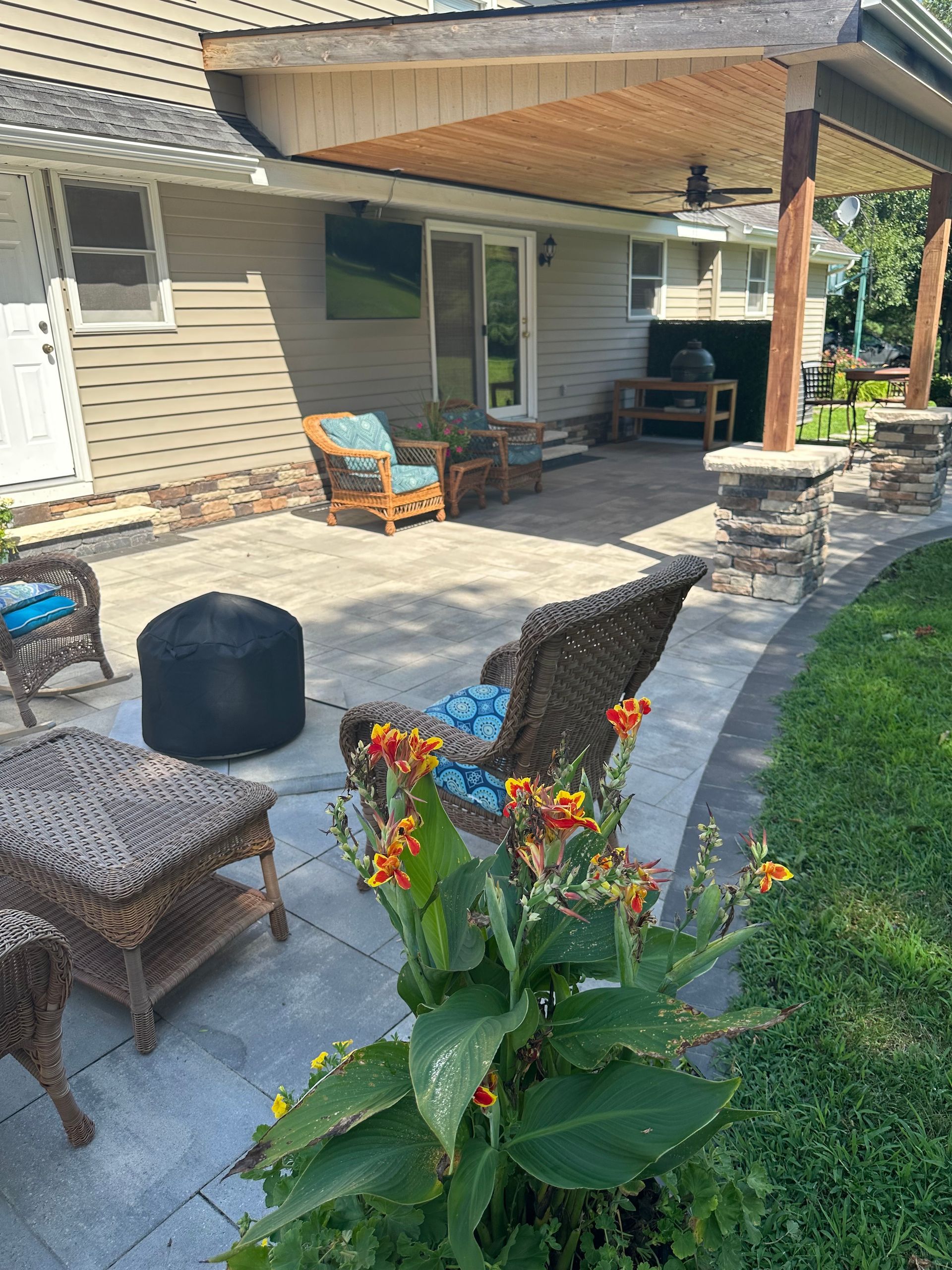 Patio with seating under a covered area and landscaping with flowers in the foreground.