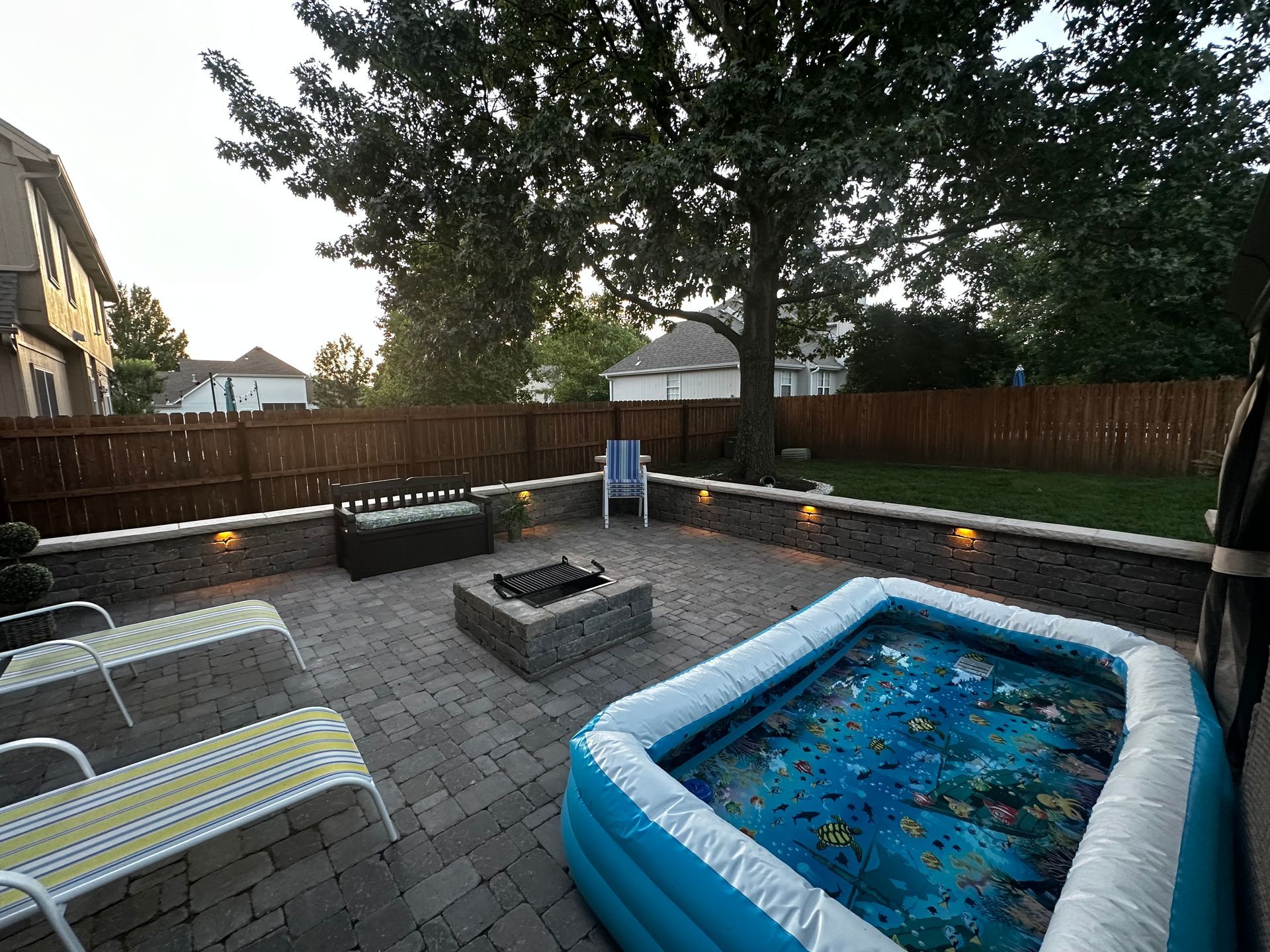 Patio with fire pit, inflatable pool, seating, and a brick wall with lights.