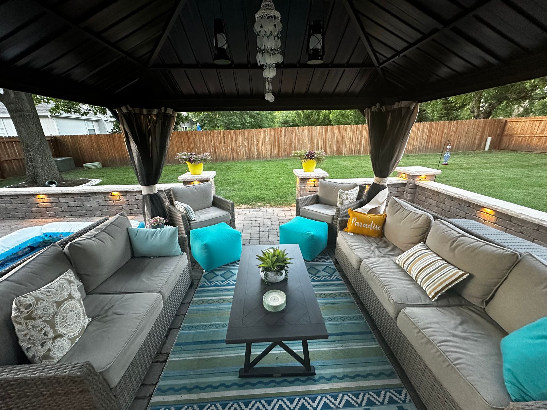 Outdoor patio with gray couches, blue rug, and black coffee table under a gazebo.